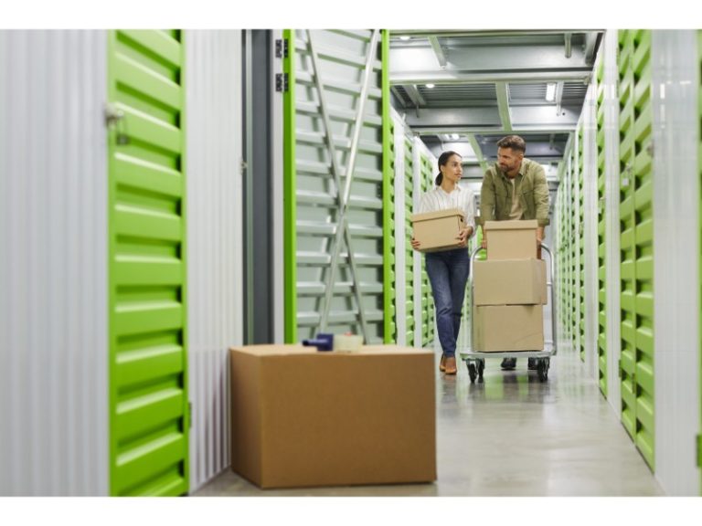 Una pareja caminando por un pasillo de almacenamiento, llevando cajas con un carrito