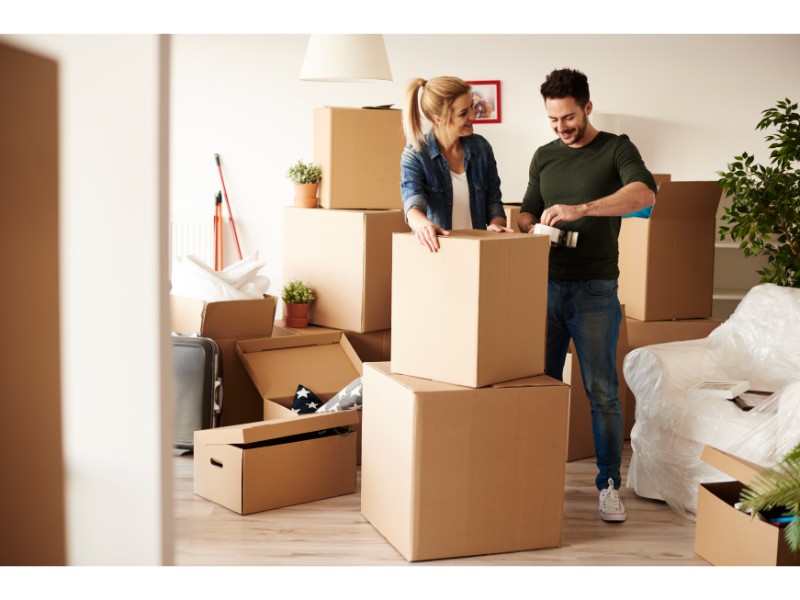 Una pareja sellando cajas mientras desempacan en su nueva casa.