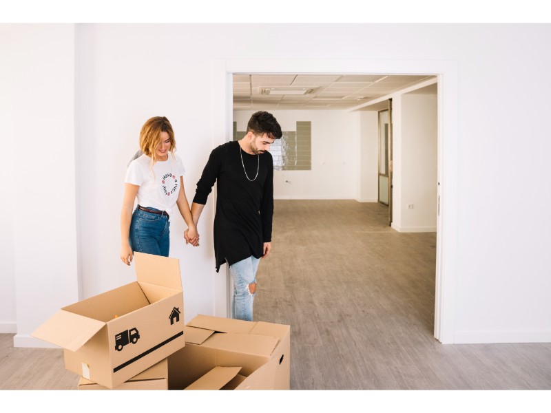 ChatGPT Plus La imagen muestra a una pareja de personas caminando tomadas de la mano en un espacio vacío. Están cerca de un par de cajas de mudanza con dibujos de camiones en ellas. El lugar parece ser una oficina o un apartamento recién desocupado, con paredes blancas y pisos de madera.